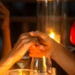 Couple on a romantic date holding hands above a candle lit dinner